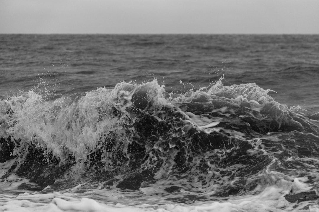 Black and white photo of the sea, with waves crashing against each other. The rough water creates splashes that create an abstract pattern in front of them. In background is dark blue ocean. Captured using Fujifilm XT4 camera with aperture f/8 for sharp focus on wave. High resolution photography, stock quality –ar 128:85