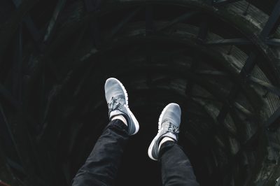 A person wearing white sneakers is standing on the edge of an abyss, with black jeans and gray shoes, looking down at their feet from above. The perspective includes low angle shots, dark tones, wideangle lenses, high contrast lighting, fast shutter speed, full body photos, loneliness.,,in --ar 128:85