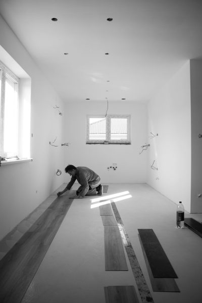 A worker laying parquet in an empty modern house, black and white photography, wide shot, unsplash photography style, in the style of unsplash. --ar 85:128