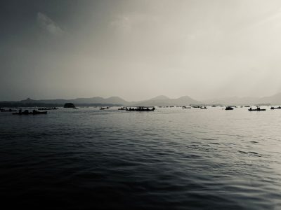 In the distance, there is an endless sea with boats floating on it. In front of them lies West Lake in Hangzhou and distant mountains. The sky above has dark clouds. There was no one around, only fishingmen were working at their fishermen's seats. A black and white photo captures this serene scene. --ar 4:3