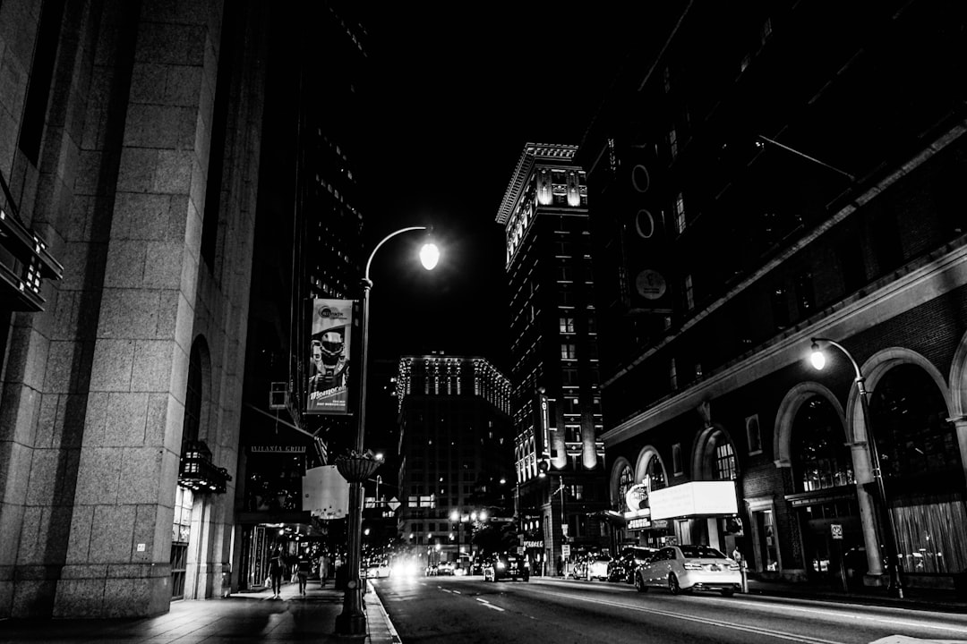 Black and white street photography of downtown Grand Rapids, featuring city lights, buildings, streets, and night time scenes, street lamps, cars driving down the road, billboards, with a low angle, wide shot perspective, in the hyper realistic, hyper detailed, high definition, high resolution style. –ar 128:85