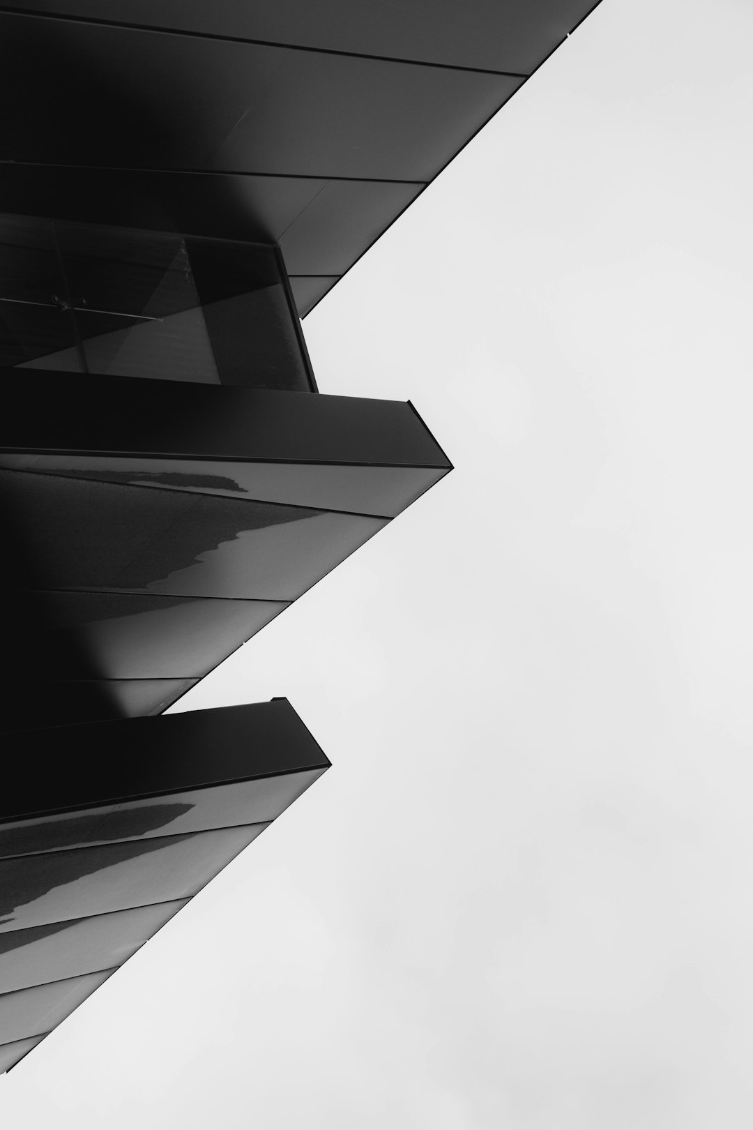 Black and white photograph of the corner detail of an office building with angular edges and a sleek design. The architectural photography features an overcast sky with shadow play and high contrast. Sharp focus is on the details with a monochromatic palette showing the modern architecture in a minimalist style, like a photoshoot for an architectural magazine. –ar 85:128