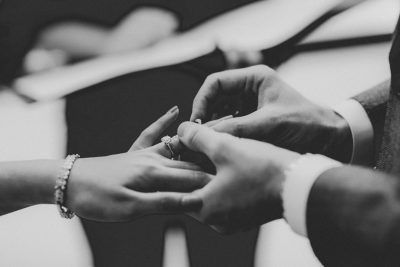 Photograph of hands exchanging rings during a wedding ceremony, capturing detailed expressions and emotions in black and white. The scene is captured from an extreme closeup perspective, focusing on intricate details like jewelry or nail polish. This photo was taken with a Canon EOS5D Mark III camera using Fujifilm Provia film stock in the style of anonymous photographers. --ar 128:85