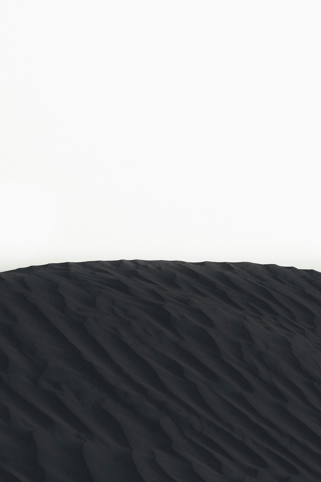 A white background with a black sand dune in the foreground, minimalistic, ultra realistic photography –ar 85:128