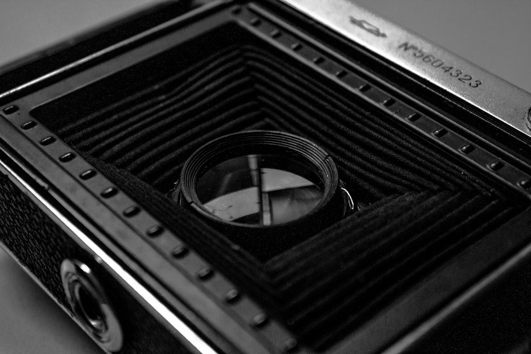 Black and white photograph of the inside of an old film camera, focusing on its intricate metal construction with a visible metal frame, lens, and cover plate. The background is a plain black to highlight details like ridges in the metal or patterns on fabric covering parts where cameras would be placed during shooting. This closeup shot captures elements that make up classic photography equipment in the style of classic photography. –ar 128:85