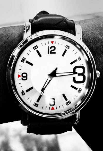 A watch on the wrist, black and white photography, macro shot, simple background, clean background, high resolution, high quality, high detail, high contrast, HDR, raw photo, no people in the picture, no hands visible in the photograph, no fingers showing off from the clock face, only one hand is seen, simple design of the watch with a leather strap, white numbers for time and a silver body frame, red marks at each hour mark on the dials, clear focus, professional photography, in the style of minimalist black and white photography. --ar 87:128