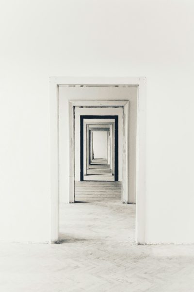 A minimalist composition of an empty room with white walls and floors, featuring multiple doorways leading to different rooms, creating the illusion that one is walking through endless doors. The overall effect should be a sense of disoriented time travel or infinite mirrors, evoking feelings of curiosity and surrealism in the style of surrealist artists. --ar 85:128