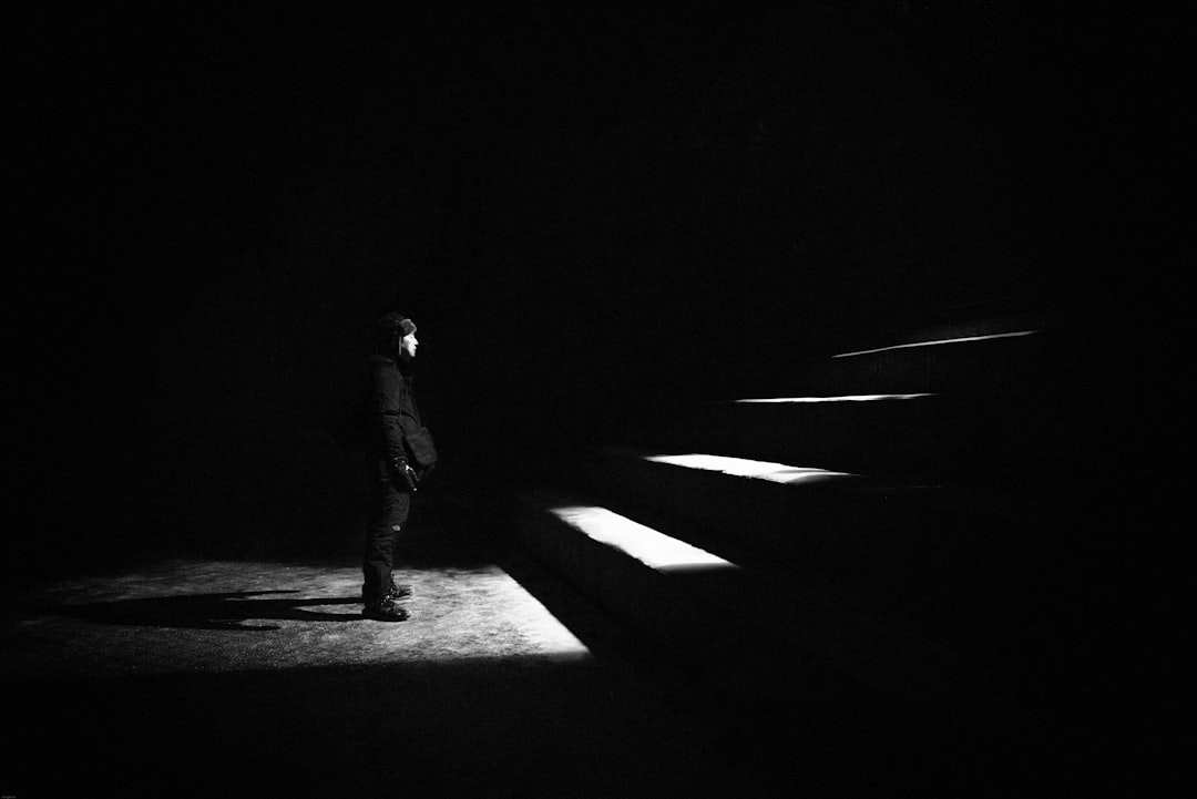 In the dark, there was only one person standing on the stage with stairs in front of him, in a side view, long shot. A spotlight and soft light illuminated his face against a minimalist background, captured in the style of black and white photography with a Leica lens. The man’s eyes glowed as if he had seen something incredible. –ar 128:85