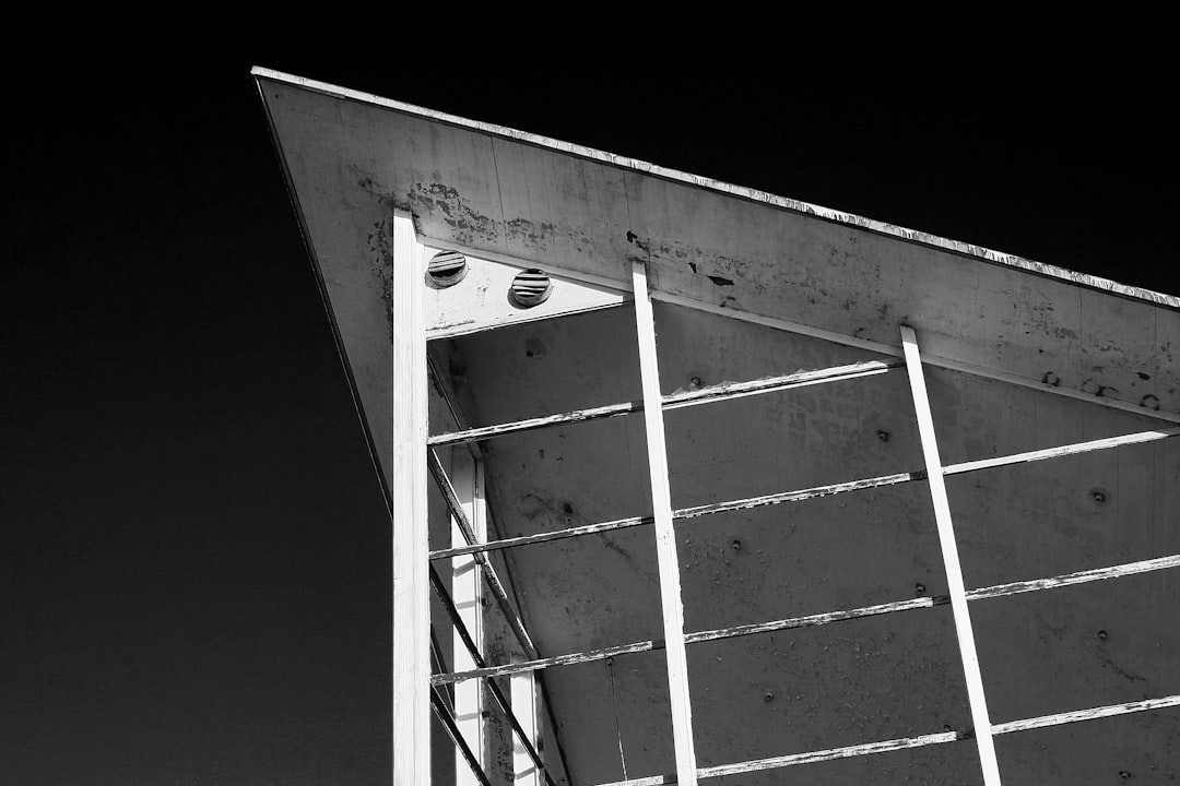 A black and white photo of the corner roof line of an industrial building with concrete panels. The left side is slightly slanted forward while on top there are two air mattresses for skydivers and above them some small round holes to hang down metal cables. The photo was shot from a low angle with a wide-angle lens, highlighting details and textures. The background should be pure black. –ar 128:85