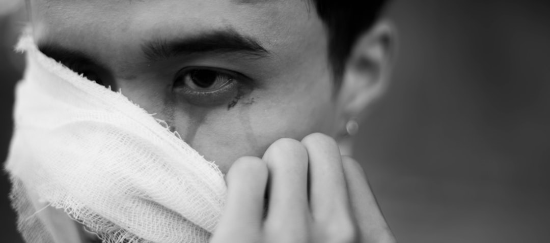 A man with his hand covering half of his face, with a white gauze bandage on one eye and nose, with black hair, in a closeup shot, with a blurred background, in the style of high resolution photography, with a Hasselblad camera XCD lens. –ar 16:7