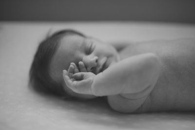 A black and white photograph of a newborn baby lying on its back, with the focus in closeup to capture their small hands or feet. The background should be simple and neutral for easy viewing. This photo was taken in the style of Nikon camera, 85mm f/2.0 lens, with a shallow depth of field. --ar 128:85