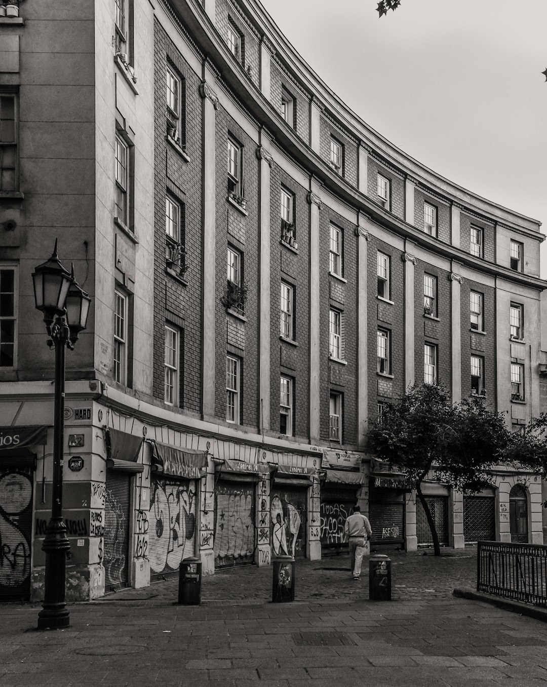 A street corner in the centre of Madrid with many white and gray buildings, some slightly curved on one side. It has an old building that is black and white with graffiti. There’s no people around. Photographic quality. –ar 51:64