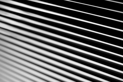 Closeup of horizontal lines on blinds, creating an abstract pattern with monochrome shades in high contrast with a shallow depth of field. A Nikon D850 was used to capture detailed texture and sharpness, focusing on the play between light and shadow. The negative space was focused on to create visual harmony. --ar 128:85