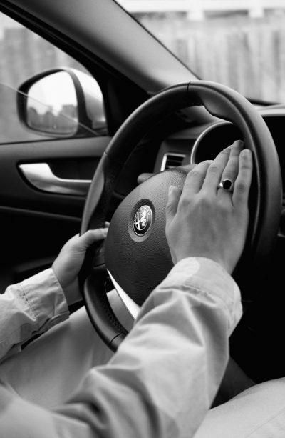 Black and white photography of hands holding the steering wheel driving in an Alfa Romeo car, in the style of Algaer, taken with a Leica M6 and Summilux f/2.8 lens. --ar 83:128