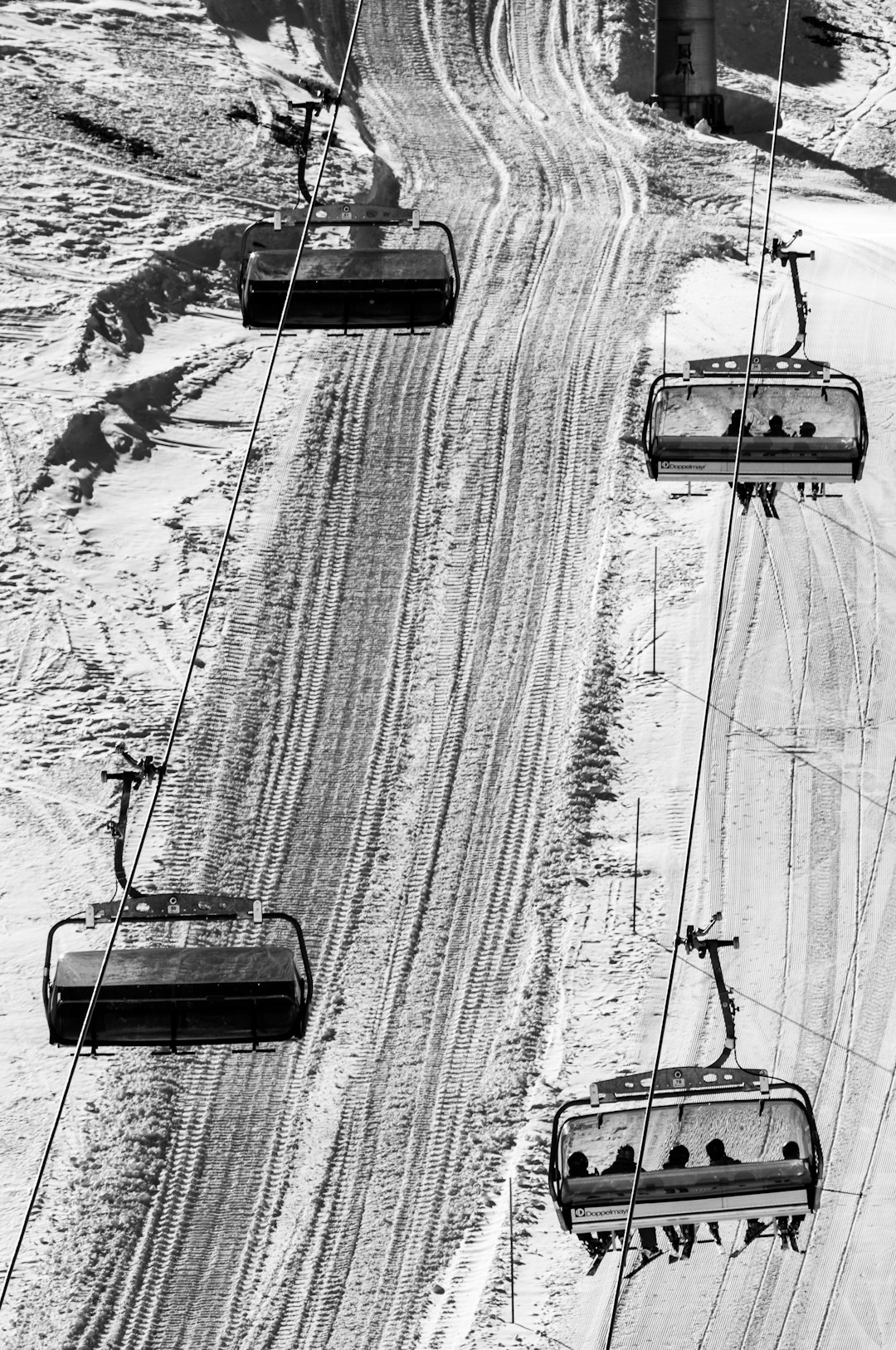 black and white photo of skiers on chair lift, ski slopes, snowing, ski trails in the air, aerial view, ski resort architecture photography, high contrast, hyper realistic, detailed textures, in the style of hyper realistic. –ar 85:128