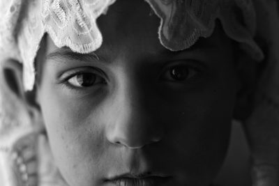 A young boy wearing a white lace headscarf in a closeup portrait, monochrome, soft light and shadow, mysterious atmosphere, clear details of the face, sad expression. in the style of monochrome. --ar 128:85