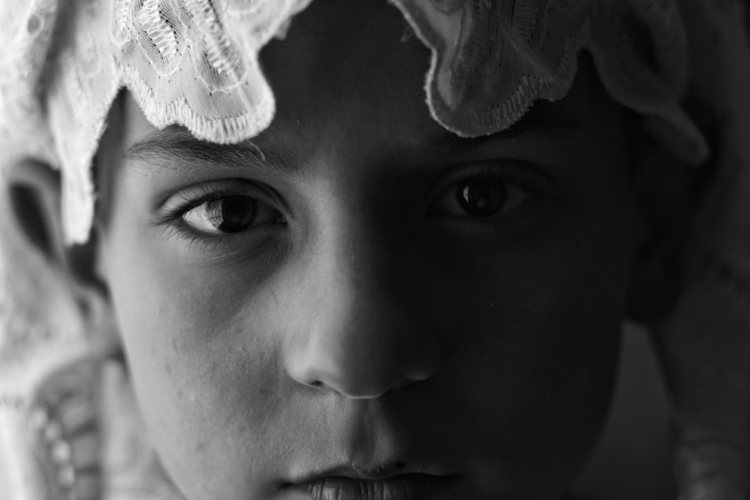 A young boy wearing a white lace headscarf in a closeup portrait, monochrome, soft light and shadow, mysterious atmosphere, clear details of the face, sad expression. in the style of monochrome. –ar 128:85