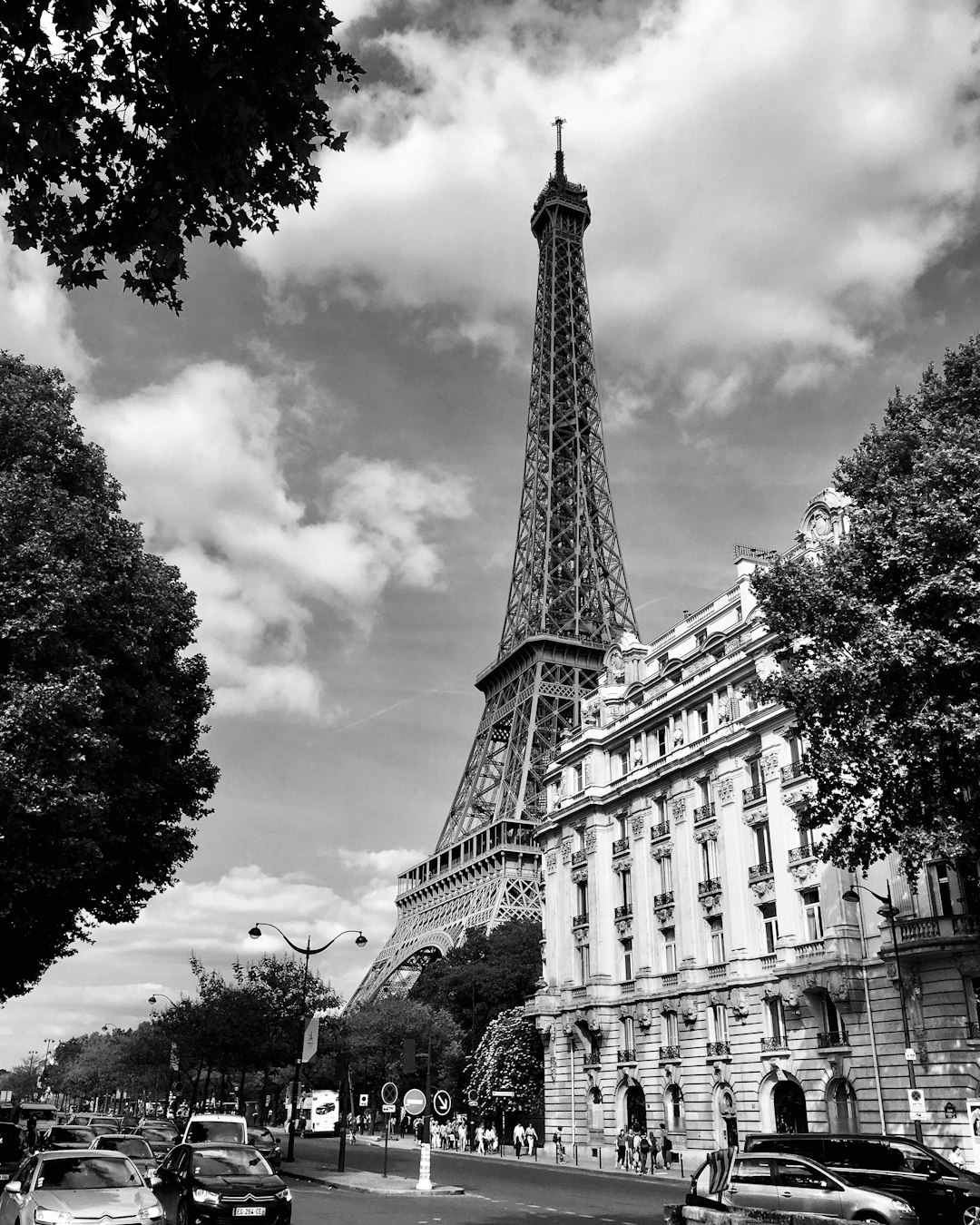 Eiffel Tower in Paris, black and white photo, sunny day, street view, cars on the road, people walking along buildings, trees around, clouds in the sky, building architecture details, Parisian style, iconic landmark of French culture and history, high resolution, detailed textures, architectural photography, professional color grading, depth of field, realism, in the style of architectural photography. –ar 51:64