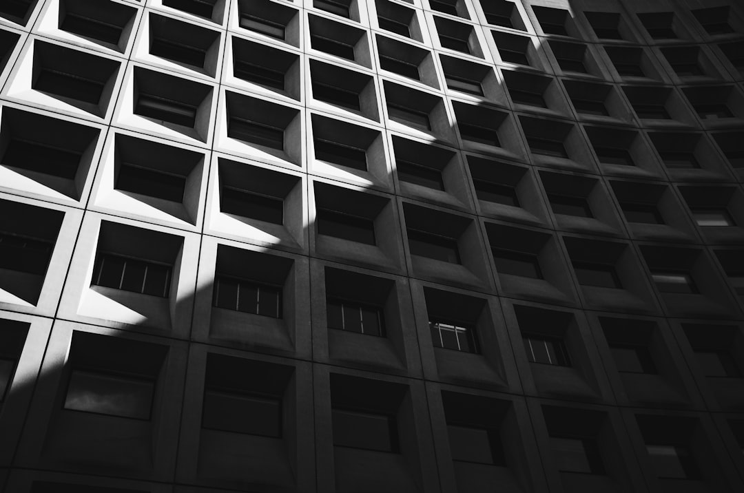 Black and white photograph of the facade of an office building in downtown San Francisco, geometric pattern on concrete walls, sunlight casting shadows across the surface, high detail –ar 32:21