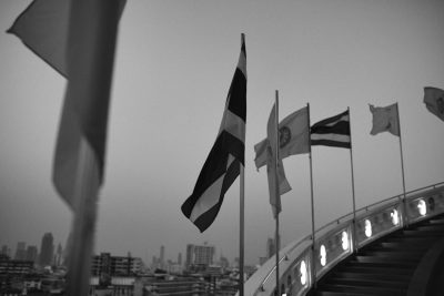 Black and white photo of flags flying in Bangkok, shot on Leica M6 with Fujifilm film stock in the style of no particular artist. --ar 128:85