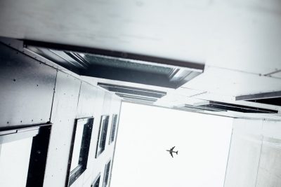 A close-up shot of an airplane flying over the roof, taken from inside a one-floor building with black and white color grading, creating a sense of depth in the composition. The perspective is looking up at the plane through window frames at ceiling level. The scene captures a contemporary architectural style with minimalist design elements, adding to its modern feel. --ar 128:85