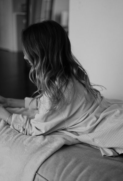 Black and white photo of a woman in a striped shirt laying on her back, watching TV, candid photography, moody aesthetic, soft light, bedroom, long hair, natural skin, no makeup, minimalist style, in the style of minimalist style. --ar 43:64