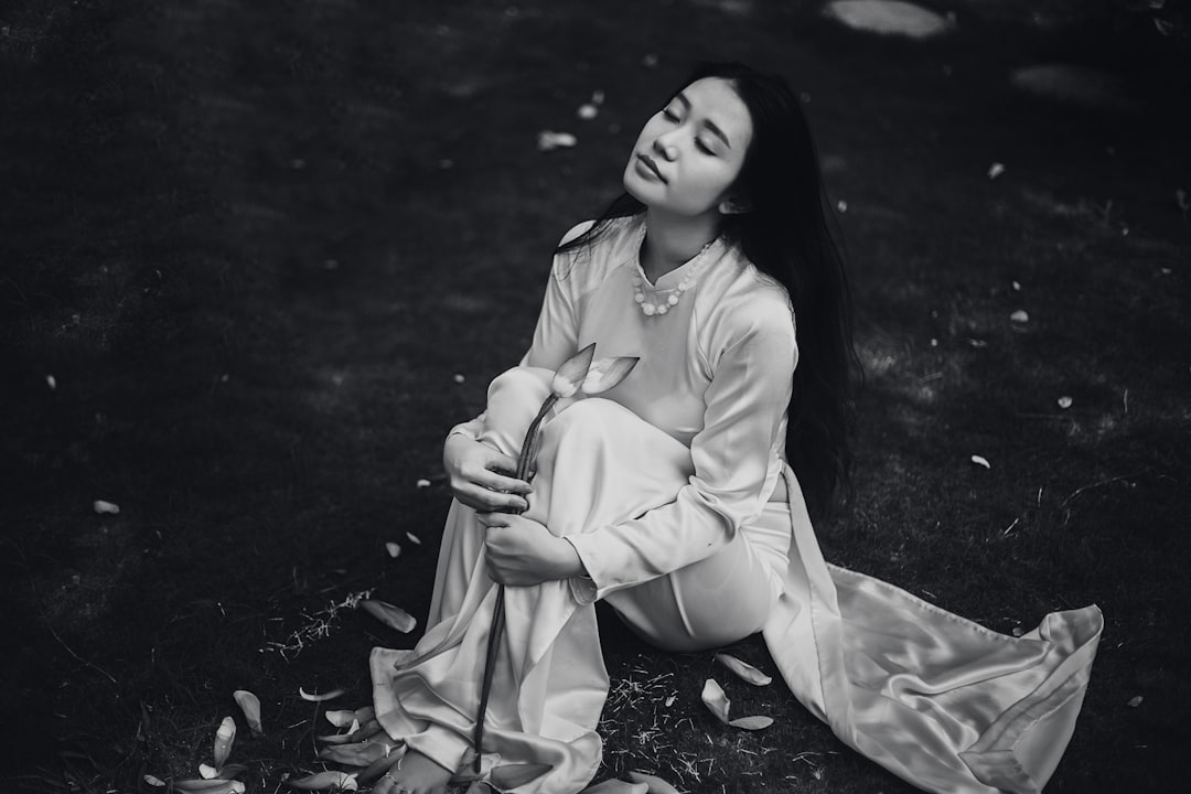 A black and white photo of an Asian woman wearing long satin pajamas, sitting on the grass in a park with closed eyes, holding a lotus flower in the style of [Ansel Adams](https://goo.gl/search?artist%20Ansel%20Adams). –ar 128:85