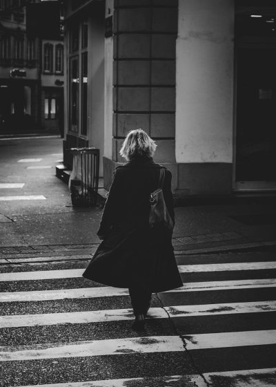 Black and white photography of blond woman walking in the streets, streetstyle , wearing coat, crosswalk, Sony A7 III --ar 91:128