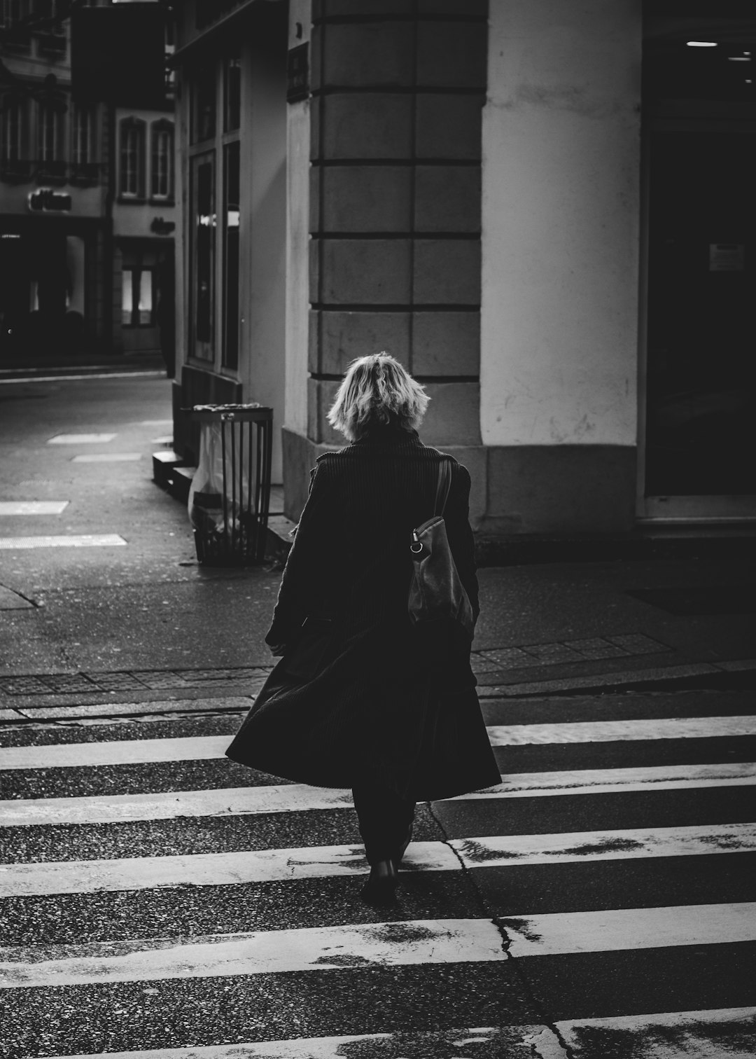 Black and white photography of blond woman walking in the streets, streetstyle , wearing coat, crosswalk, Sony A7 III –ar 91:128