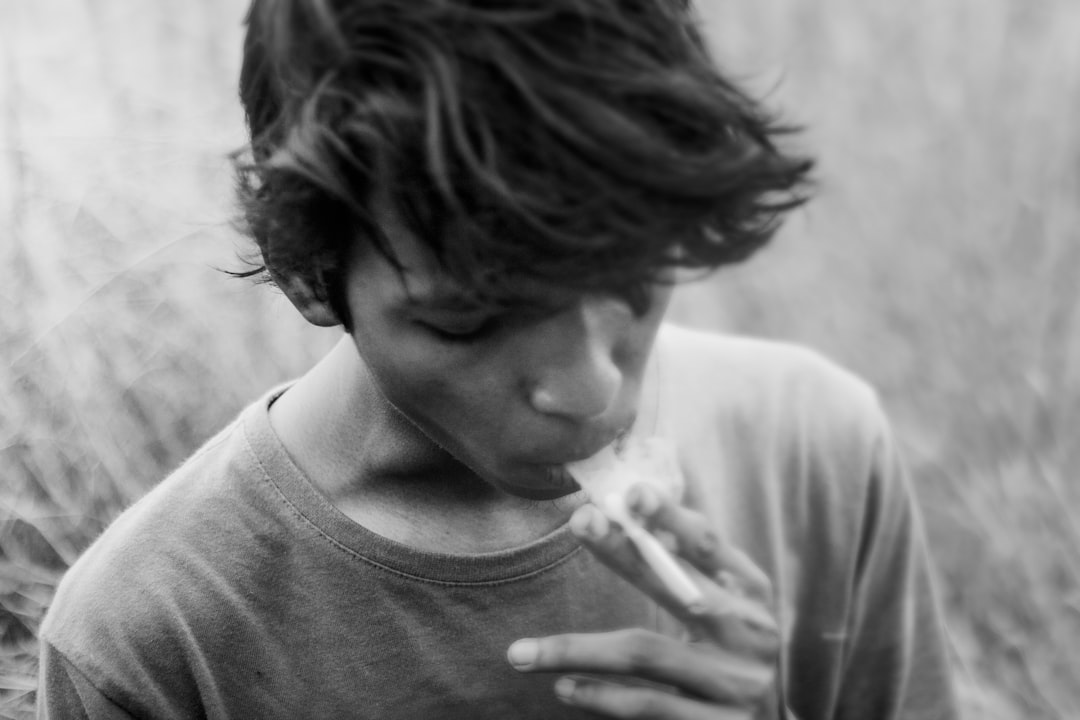 A teenage boy smoking in natural light, in the style of fujifilm XTRA black and white photography, grainy. –ar 128:85