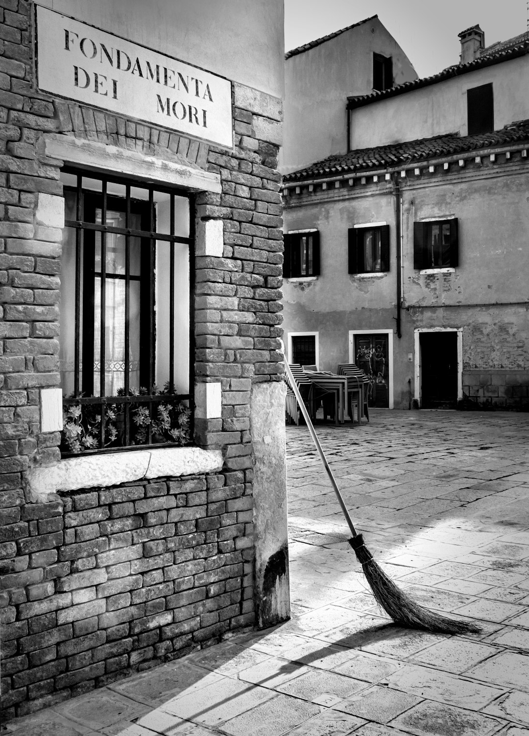 A broom leaning against the wall of an old building in Venice, Italy with “FONdec nova de M” written on it, in the style of black and white photography on a sunny day street scene architectural photography. –ar 23:32