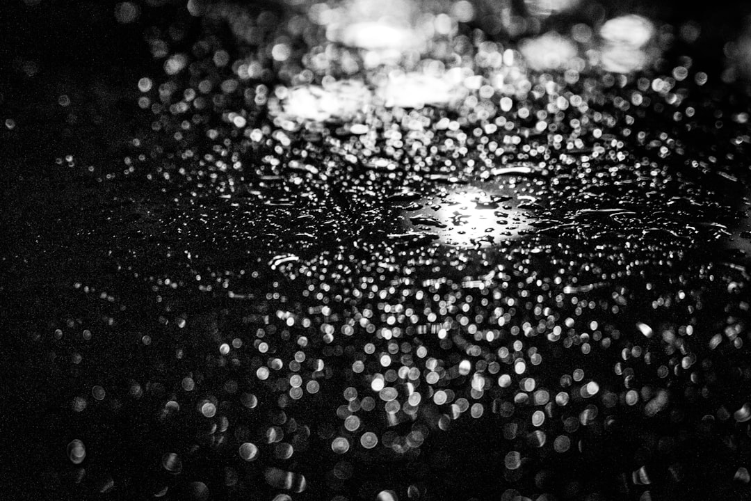 Black and white photography of raindrops on a car window, reflections, night time, grainy texture in the style of night time. –ar 128:85