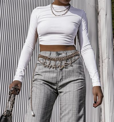 African American woman wearing a white long sleeve shirt, grey plaid straight leg jeans with chains and a belt in the style of a streetwear aesthetic. The look is cute and dreamy with photorealistic detail and a sleek metallic finish for an urban grunge look. --ar 15:16