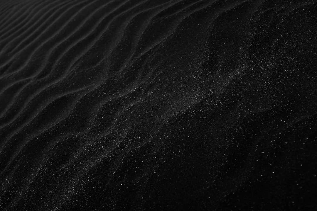 Black sand texture background. Sand ripples in the wind. Dark desert dunes with a starry night sky. A dark sand pattern. A minimalist black and white design. A dark abstract texture. A shiny grainy sand surface in the style of starry night. –ar 128:85