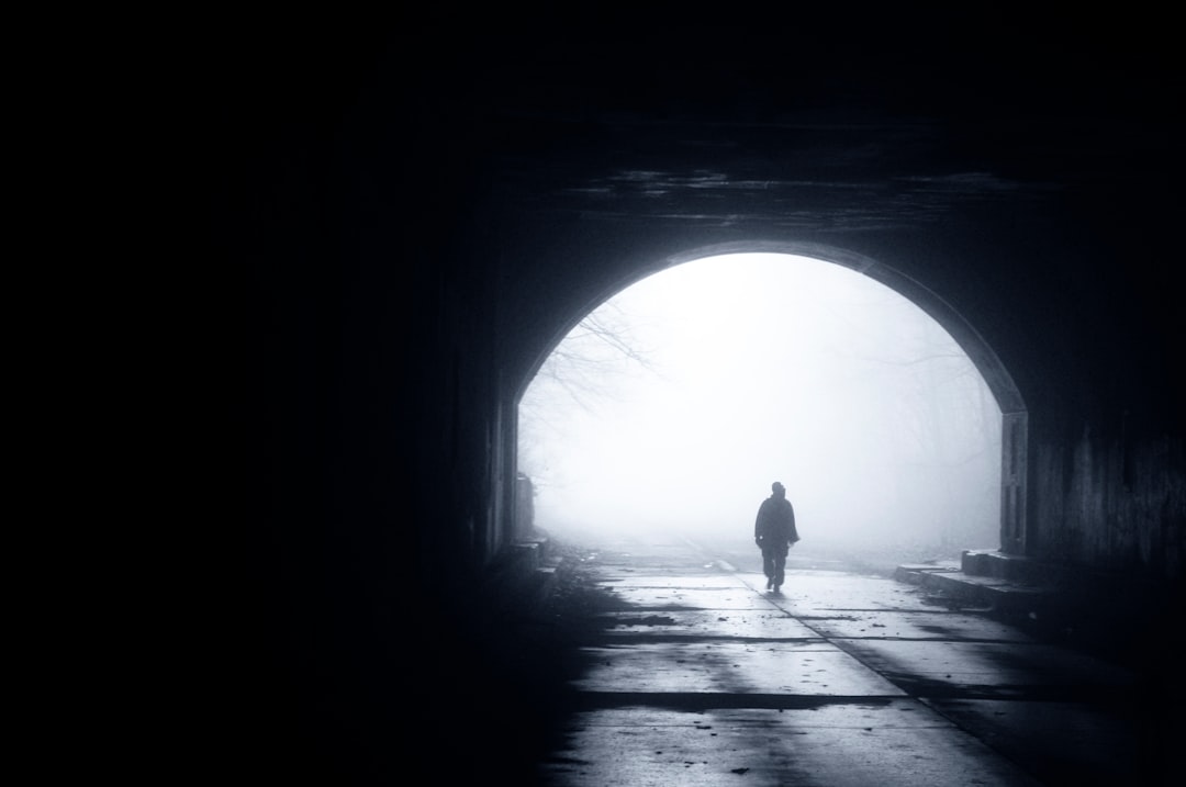 A man walking in a tunnel, with a foggy background, as a silhouette, alone and isolated, in black and white, with a dark mood, in the style of high resolution photography. –ar 128:85