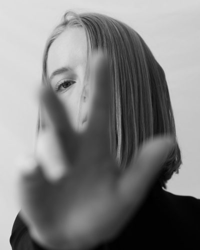 A woman with straight hair is holding her hand out in front of the camera, making a stop sign gesture. Her face can be seen from behind and she has a medium length bob haircut. The background should be white with the focus on her hand so that it stands out against everything else. The shot was taken in the style of Sony Alpha A7 III with a black & white filter. --ar 51:64