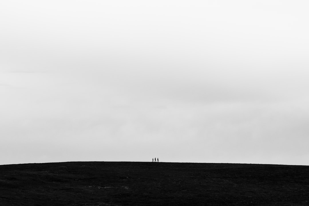 Black and white minimalistic photo depicting the silhouettes of three people standing on top of an endless black hill against a grey sky, taken with a medium shot using a Fujifilm X-H2S camera. –ar 128:85