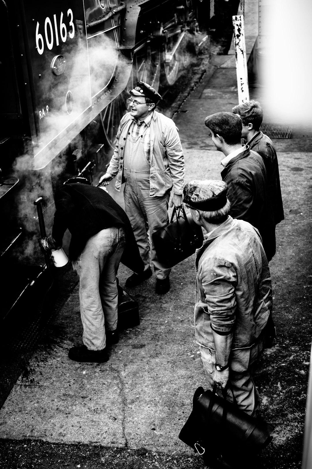 black and white photo of three men in work getting on the side off an old steam train, one is carrying his bag from which he has pulled out some small black bags of coffee beans, they stand next to each other at different angles, shot with sony alpha A7 III camera, with f/8 aperture setting, there’s smoke coming from under their feet as if it had just broken down, one man leans over the edge looking around him, one woman stands behind them talking into her phone –ar 85:128