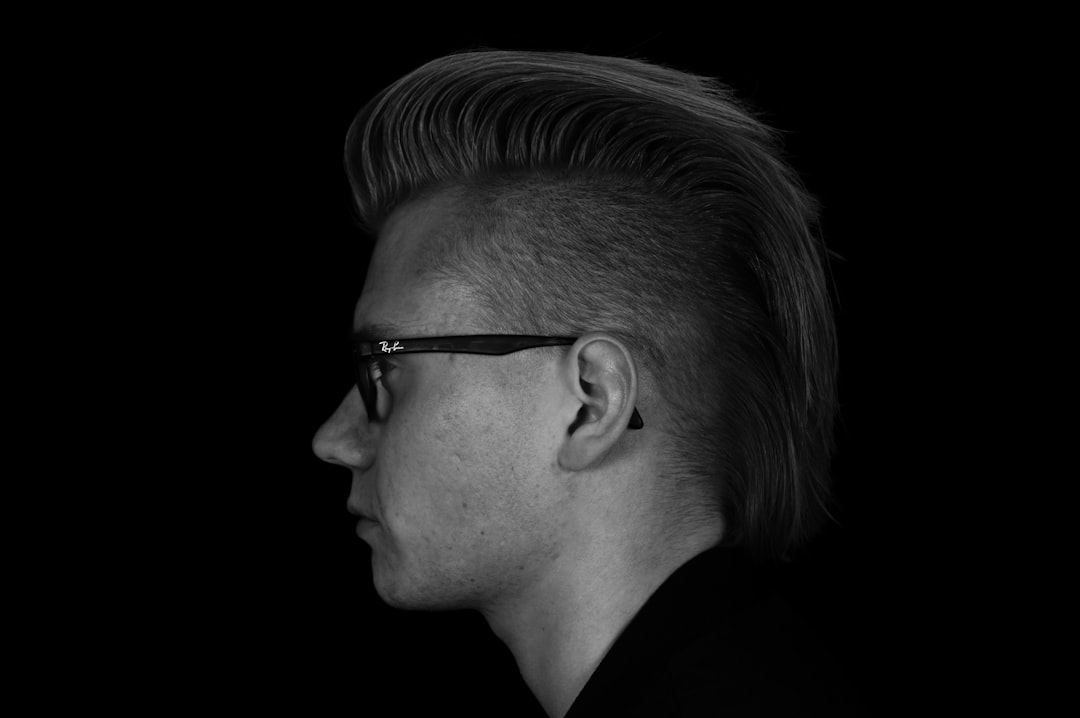 side profile of man with long mohawk hair and glasses, black background, grayscale –ar 128:85