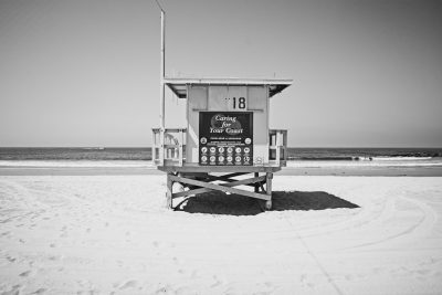 Black and white photo of lifeguard tower on beach with sign that says "Caring For Your Pointer", large number 8, ocean in background, bright sunny day, white sand, no people, shot from eye level --ar 128:85