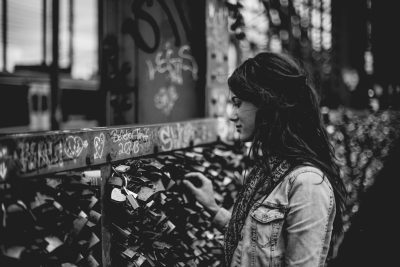 Black and white street photography of a woman looking at a heart shaped lock on a wall full of love locks, wearing a denim jacket, on a street in Berlin in the style of [Fan Ho](https://goo.gl/search?artist%20Fan%20Ho). --ar 128:85