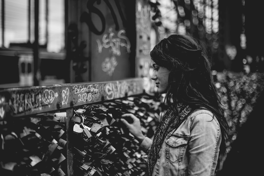 Black and white street photography of a woman looking at a heart shaped lock on a wall full of love locks, wearing a denim jacket, on a street in Berlin in the style of [Fan Ho](https://goo.gl/search?artist%20Fan%20Ho). –ar 128:85