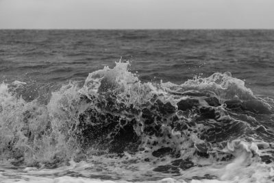 black and white photo of sea waves, taken with Canon EOS R5 at F2, ISO 4036mm, showing water splashes, with a close up view and distant horizon, rough seas, sea spray, with a distant ocean background, in the style of no particular artist. --ar 128:85