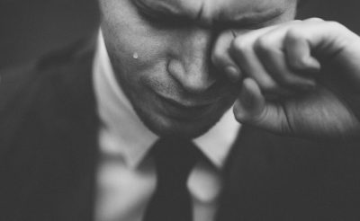 Close-up black-and-white photo of man in suit crying with his hand on face, taken with a 35mm lens. The photo appears to be in the style of a documentary photograph, capturing raw emotion. --ar 64:39