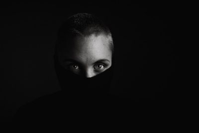 A face of a woman with short hair and a balaclava covering her eyes is barely visible in the darkness against a black background. The photography has a cinematic light, soft shadows, and high contrast in a hyper realistic style. The shot was taken in the style of an ARRIFLEX 35 BL Camera with Canon K35 prime lenses. --ar 128:85