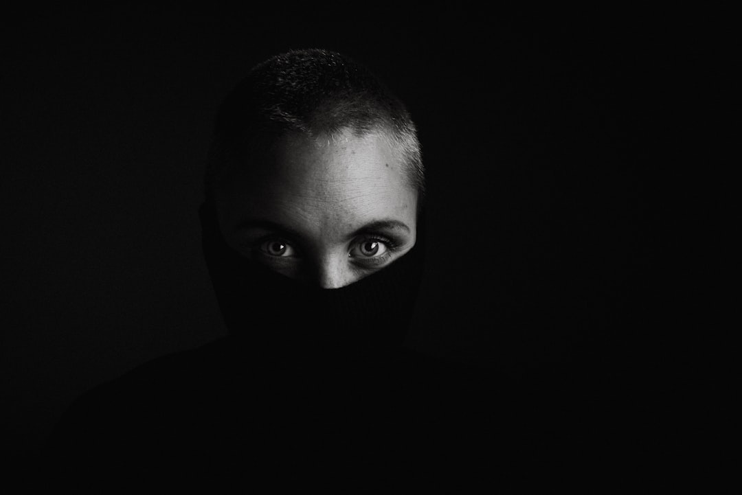 A face of a woman with short hair and a balaclava covering her eyes is barely visible in the darkness against a black background. The photography has a cinematic light, soft shadows, and high contrast in a hyper realistic style. The shot was taken in the style of an ARRIFLEX 35 BL Camera with Canon K35 prime lenses. –ar 128:85