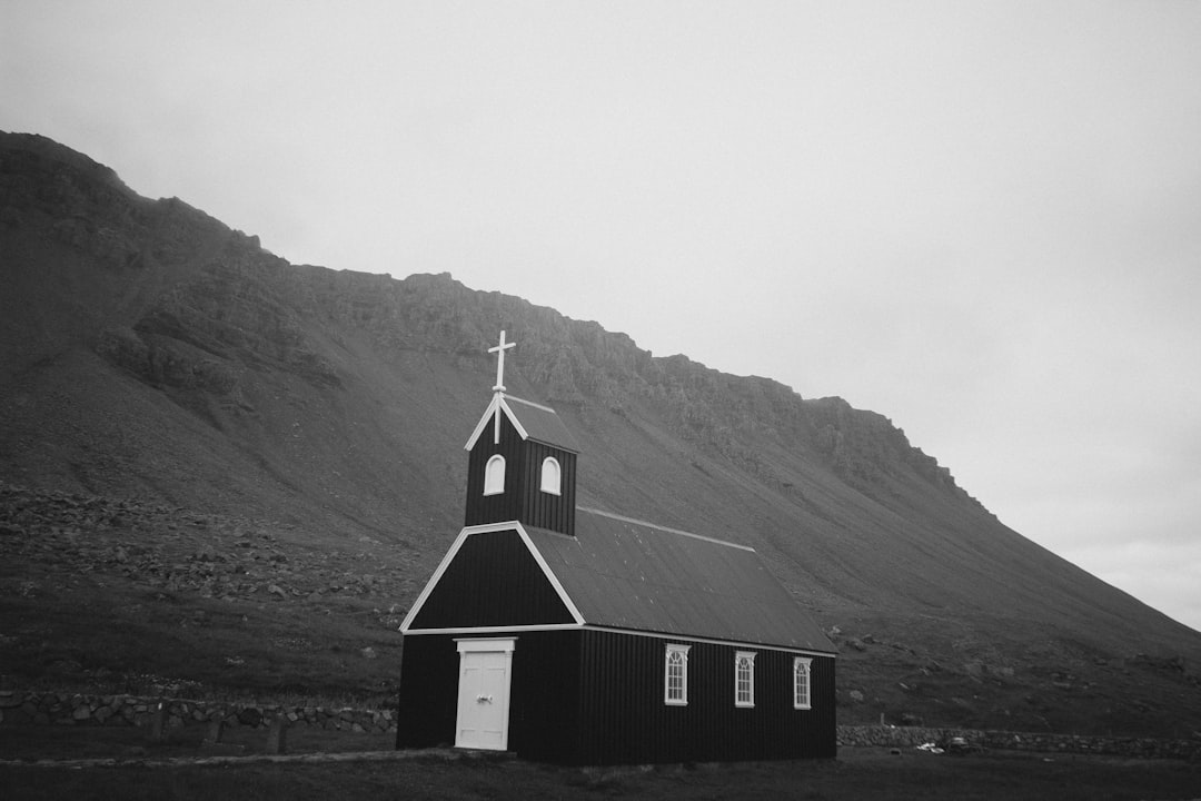 Black and white photo of a small church in Iceland. The architecture is simple with a minimalist style against a mountainous background. The photography style is reminiscent of unsplash with a black and white, grainy film filter giving it a cinematic look, as if shot with a Leica M6 camera. –ar 128:85