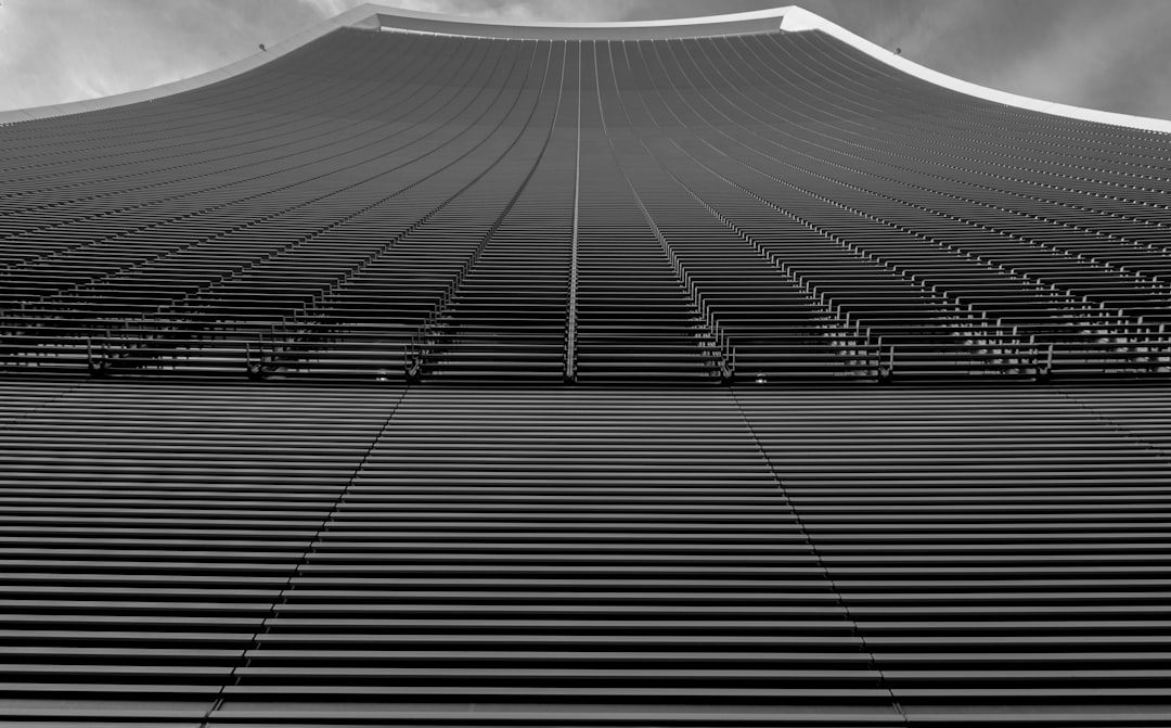 The top of the Maitama Tower in black and white, with its iconic patterned facade, features rows of vertical lines that create an elegant texture. The sky is clear above it, adding to the overall minimalist aesthetic of the building. Shot from below using a Canon EF macro lens at f/2 for sharp detail capture in the style of minimalism. –ar 128:79