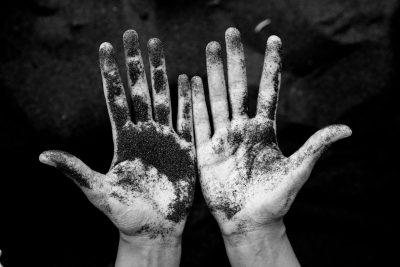 A black and white photo of two hands with black sand on the palms against a dark background. The photo has a gritty and dirty style, in the style of [Fan Ho](https://goo.gl/search?artist%20Fan%20Ho). --ar 128:85