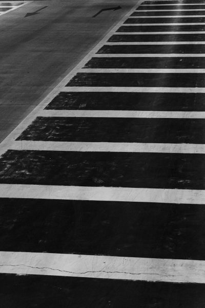 Black and white photograph of the crosswalk stripes on an empty street, capturing their contrast against the asphalt. The lines create a stark visual effect that emphasizes depth in the urban landscape. High-resolution photography with natural lighting to highlight details. A minimalistic composition focusing only on these striking painted strokes, creating a powerful yet simple aesthetic. --ar 85:128